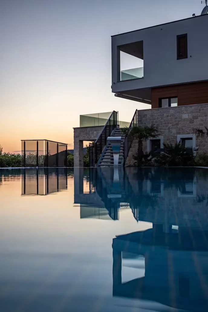 Villa konsepti: gün batımında havuza yansıyan taş cepheli villa